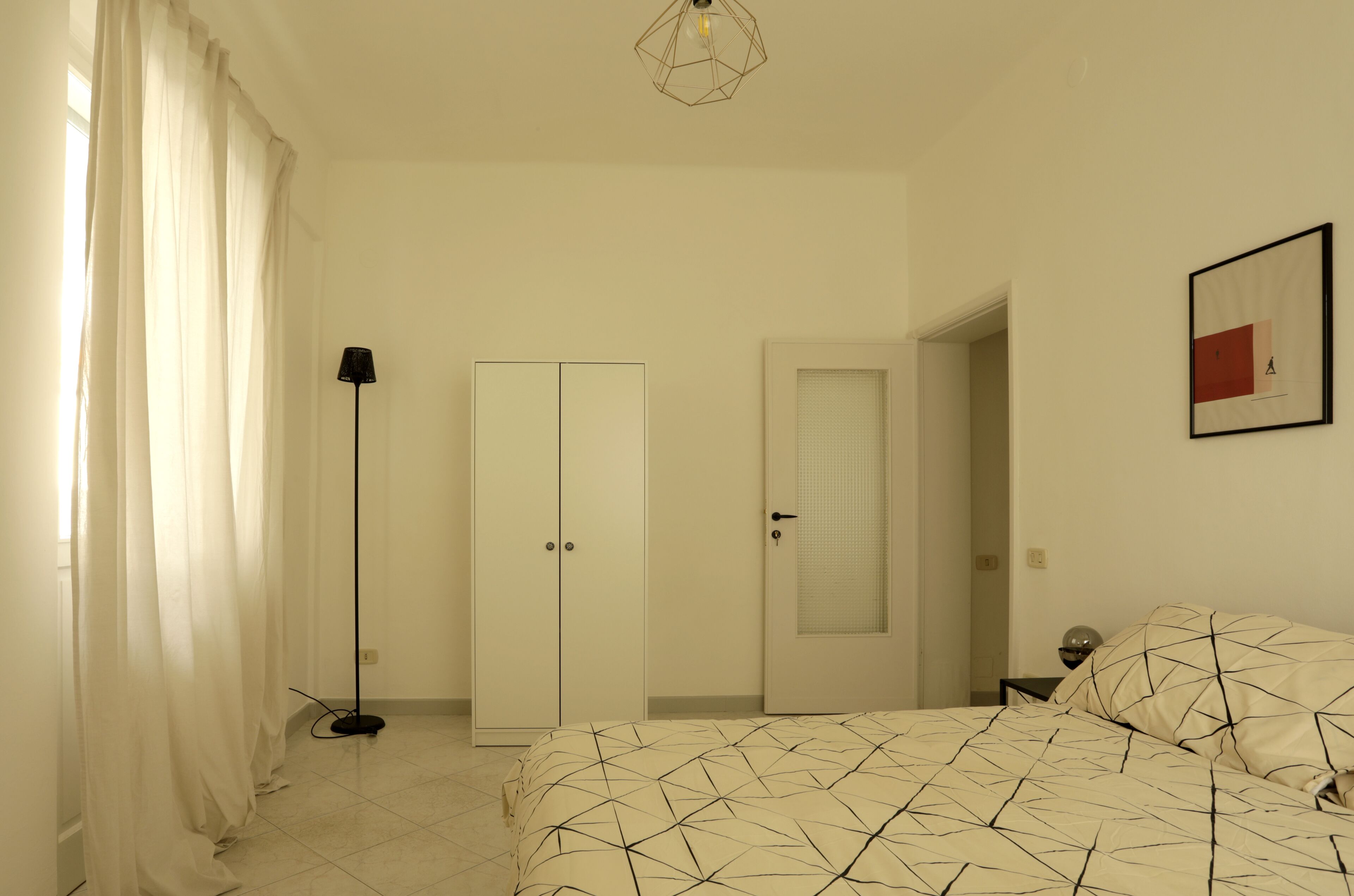 Une chambre à coucher avec un lit, une armoire, une lampe sur pied et une porte.