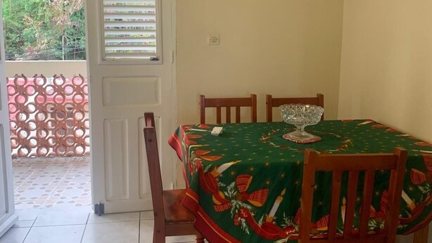 A dining area with a table set for four, a door with shutters, and a view of greenery outside. - 2-person studio with sea view (Le Marin)