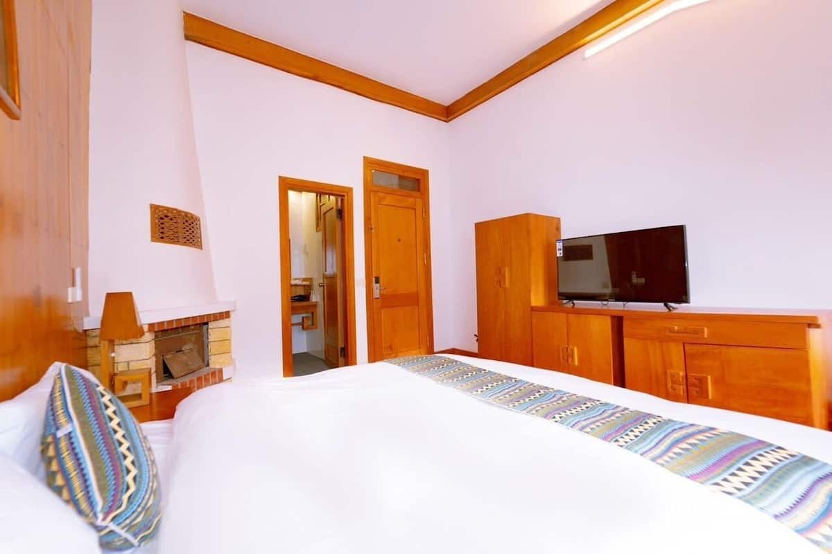 A hotel room with a bed, a television, wooden cabinets, and a fireplace.