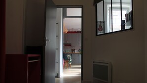 A hallway leading to a kitchen with cabinets, a dining table, and a hanging light fixture. - Appartement Centre Historique (Besançon)