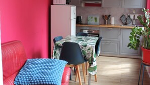 A modern kitchen with grey cabinets, a white refrigerator, and a dining area with a table and chairs. - Appartement Centre Historique (Besançon)