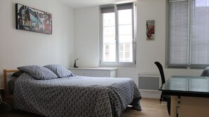 A bedroom with a bed, a desk, and a window. - Appartement Centre Historique (Besançon)