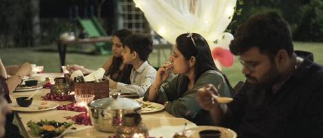 A group of people dining outdoors at night with string lights and a white canopy.