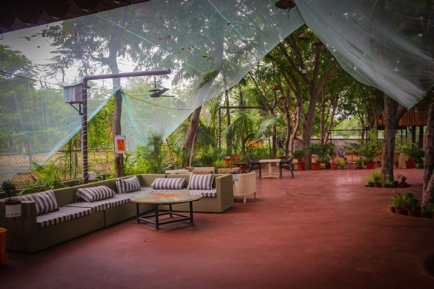 Un patio al aire libre con un área de estar cubierta, rodeado de exuberante vegetación y árboles.