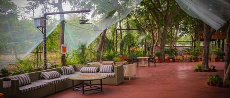 Un patio al aire libre con un área de estar cubierta, rodeado de exuberante vegetación y árboles.