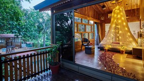 A wooden cabin with a balcony, large windows, and a canopy bed. - Visamo Nalsarovar Resort Ahmedabad (Bavla)