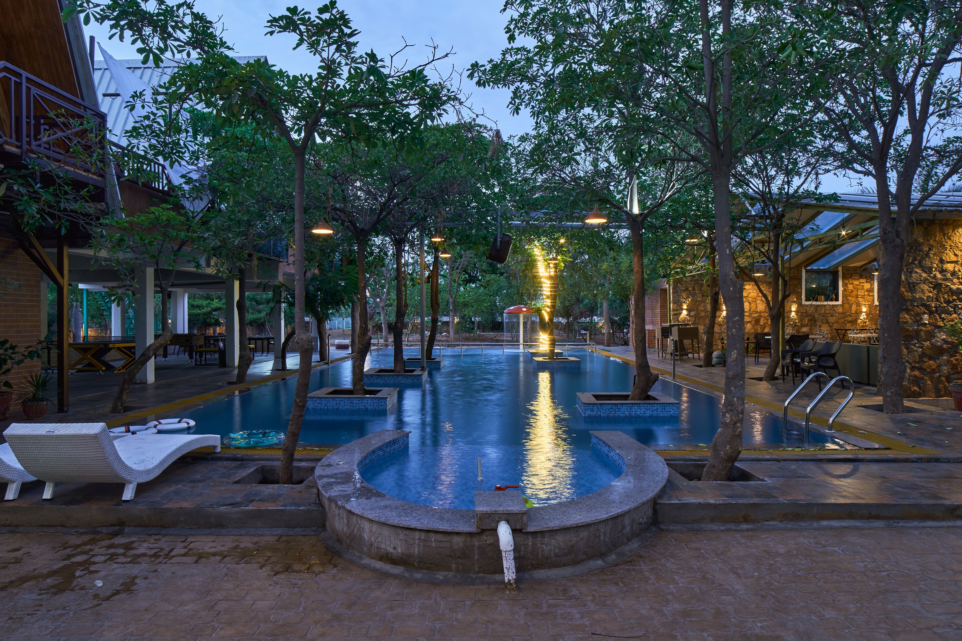 Un área de piscina con sillas de descanso, una fuente y un restaurante al fondo.