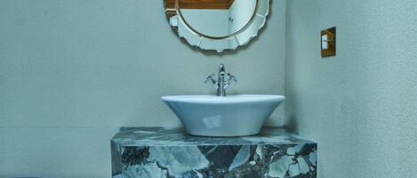 A bathroom with a wooden ceiling, a sink with a marble countertop, a decorative mirror, and a tiled floor with a geometric pattern.