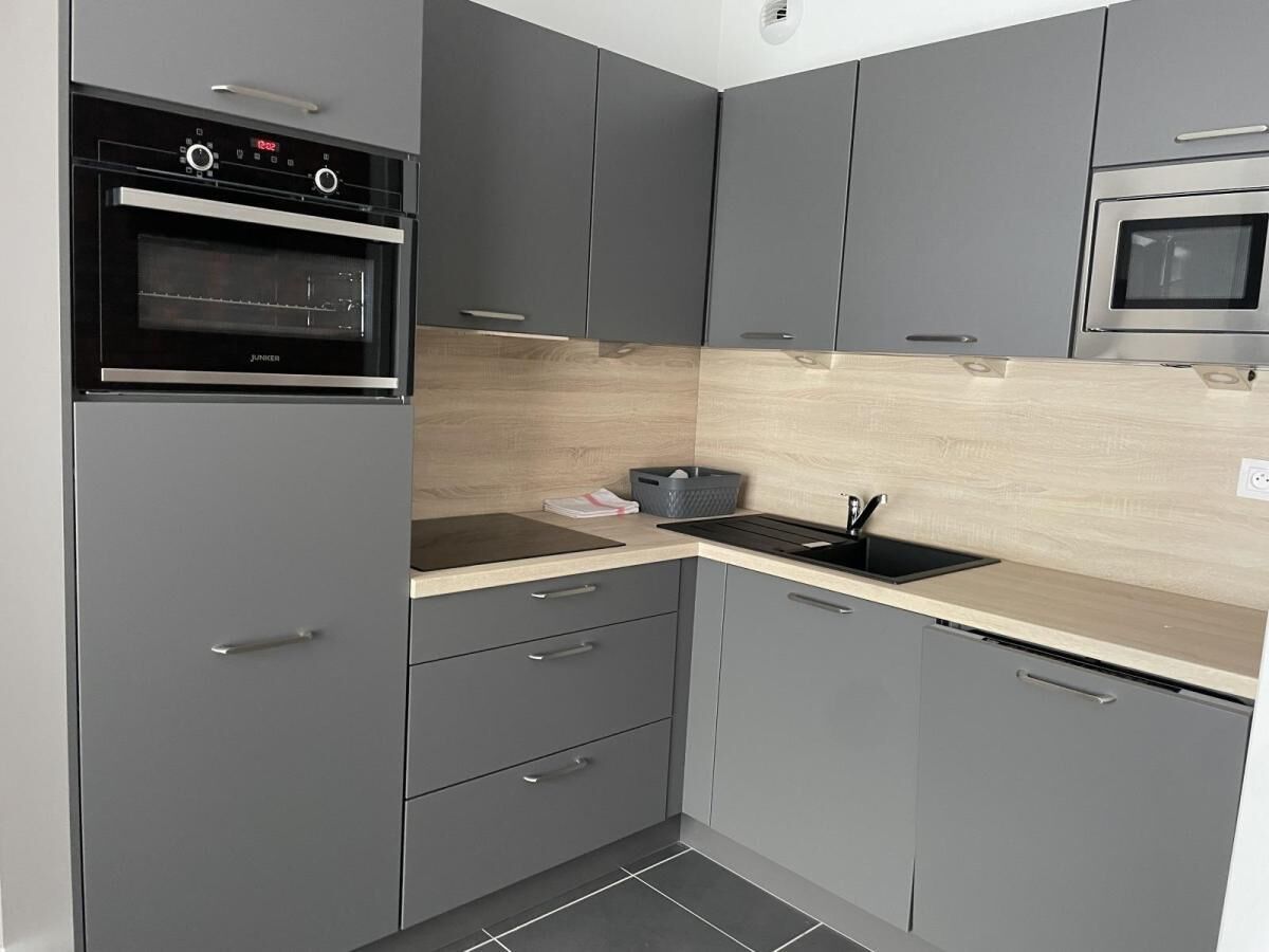Une cuisine moderne avec des armoires grises, un four encastré, un four à micro-ondes et un plan de travail en bois.
