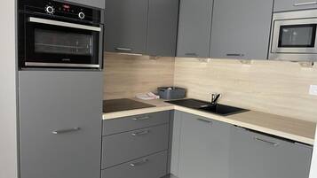Une cuisine moderne avec des armoires grises, un four encastré, un four à micro-ondes et un plan de travail en bois.