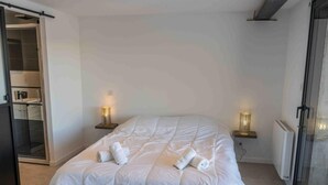 A neatly made bed with white linens and towels, two bedside lamps, and a sliding glass door leading to a shower area. - 350m from ski slopes, tv, ski locker, 51m², Les Orres (Les Orres)