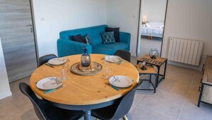 A dining area with a round wooden table set for four, a blue sofa in the background, and a small side table with a lamp. - 350m from ski slopes, tv, ski locker, 51m², Les Orres (Les Orres)