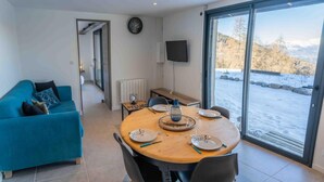 A modern living room with a blue sofa, a dining table set for four, and a large window with a snowy view. - 350m from ski slopes, tv, ski locker, 51m², Les Orres (Les Orres)
