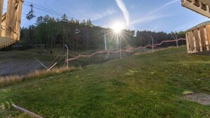 Zona verde con una estructura de madera, un telesilla y un bosque al fondo.