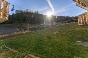 A grassy area with a wooden structure, a ski lift, and a forest in the background.