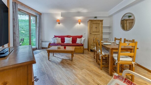 Una habitación acogedora con una mesa de comedor de madera, un sofá rojo y un televisor sobre un mueble de madera.