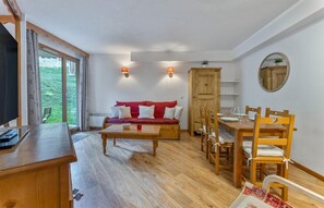Een knus vertrek met een houten eettafel, een rode bank en een televisie op een houten dressoir.