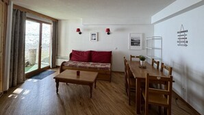 Un cuarto acogedor con piso de madera, un sofá rojo, una mesa de comedor con sillas y un ventanal con cortinas.