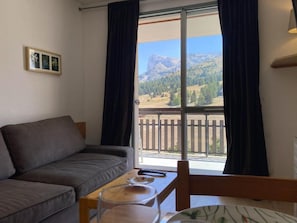 Ein Wohnzimmer mit einer Couch, einem Tisch mit einem Glas und Blick auf eine Berglandschaft vom Balkon aus.