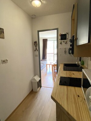 Et kompakt køkken med en træbordplade, en vask og en lille skraldespand. Der er en dør, der fører til en balkon med udsigt udad.