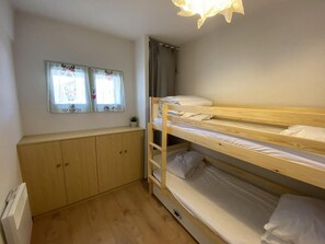 Ein Schlafraum mit Etagenbetten, einem Holzschrank und einem Fenster mit Vorhängen.