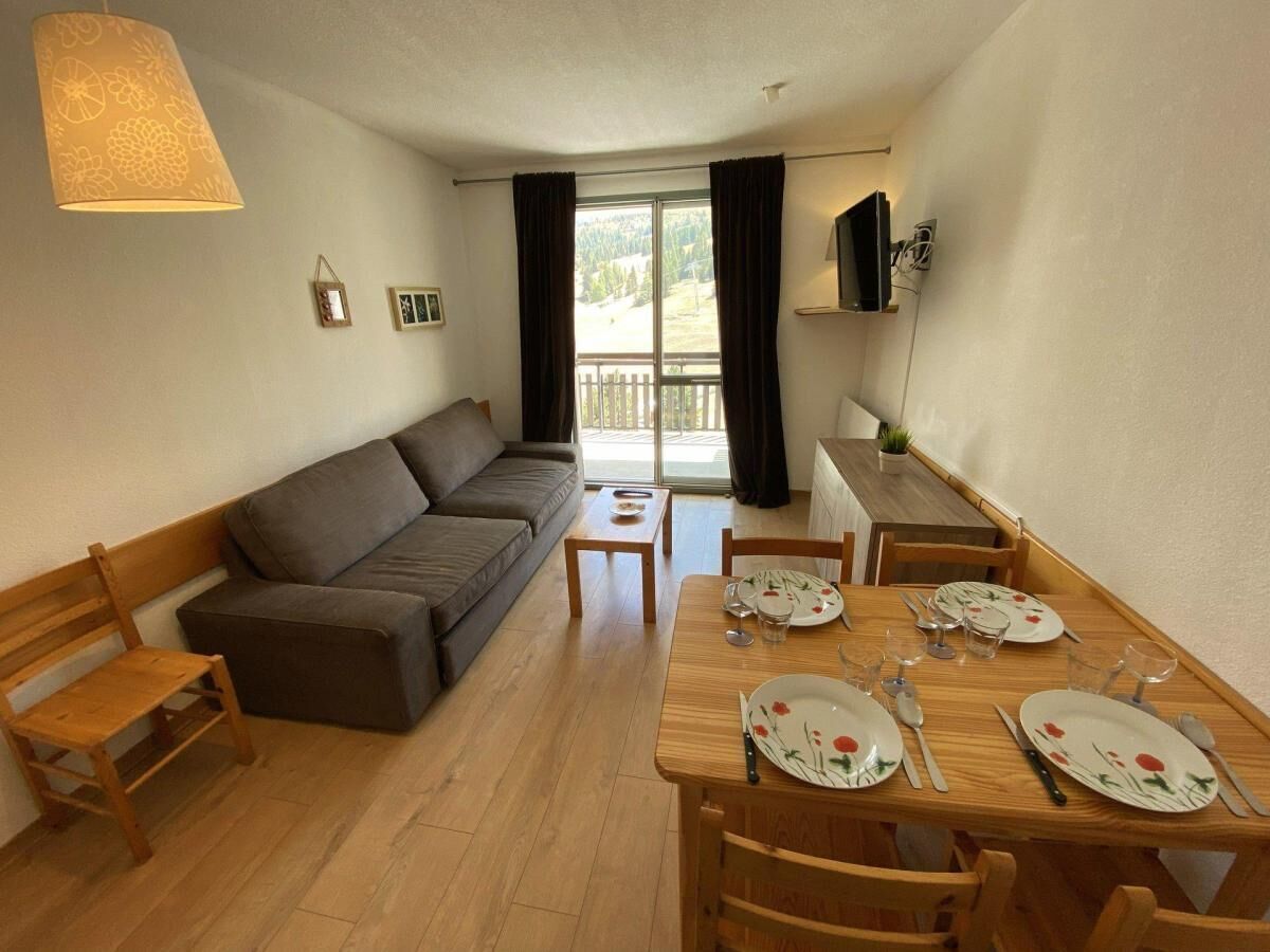 A compact living space with a sofa, dining table set for four, and a small window with curtains.