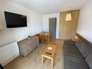 Ein Wohnzimmer mit Flachbildfernseher, einer Couch, einem Couchtisch, einem Esstisch mit Stühlen und einem Kleiderschrank.