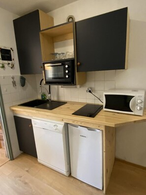 Eine kompakte Küche mit integriertem Mikrowellenherd, Geschirrspüler und einer Holz Arbeitsplatte.