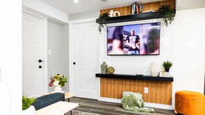 Ein modernes Wohnzimmer mit einem an der Wand montierten Flachbildfernseher, einer Holz-Akzentwand, einem grünen Kissen und einer hölzernen Bank.