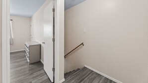 Ein Flur mit einer weißen Tür, die zu einem Zimmer führt, in dem ein weißes Regal und ein Duschvorhang zu sehen sind.