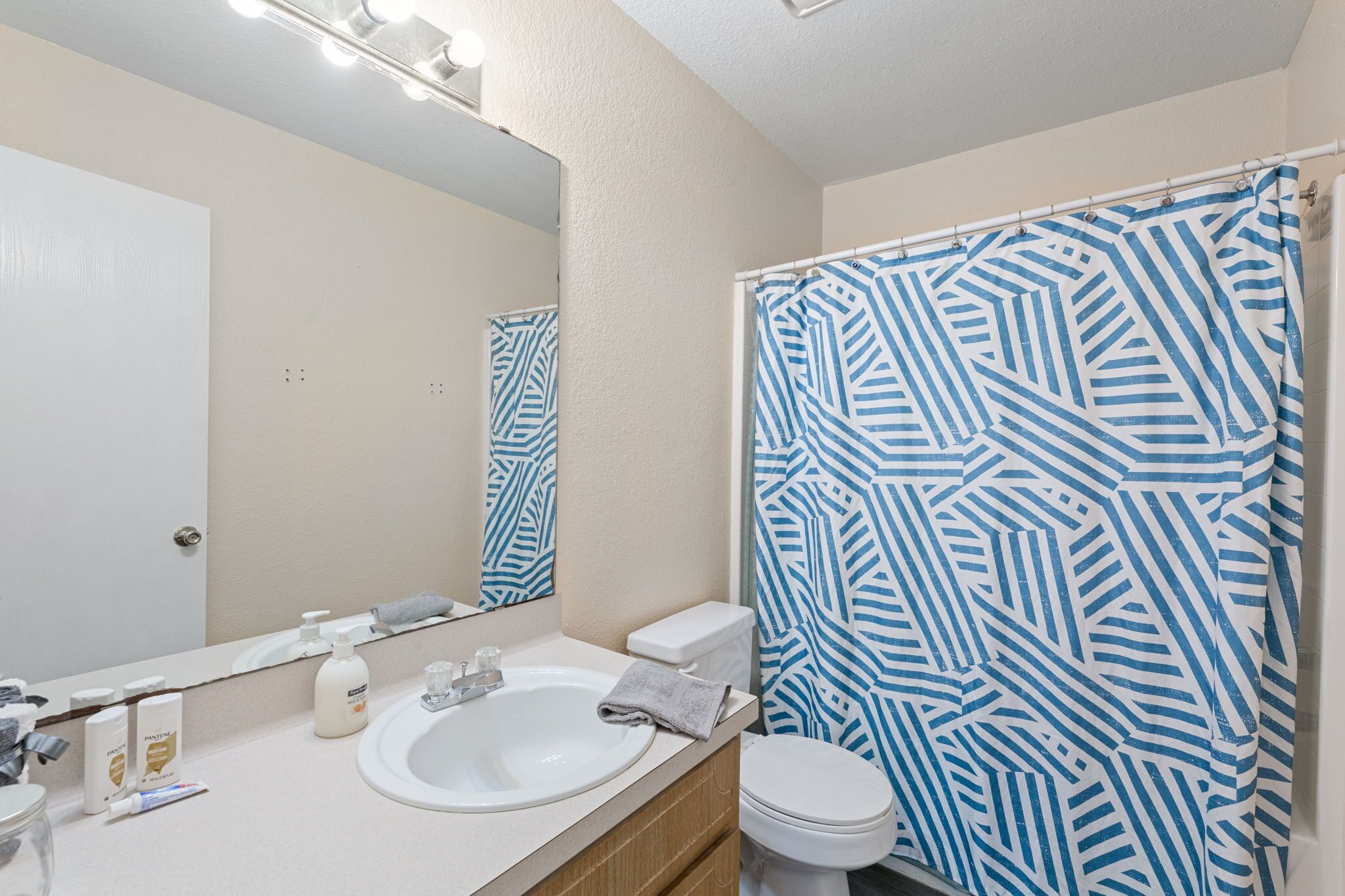 A bathroom with a white sink, mirror, and toilet. There is a shower curtain with a blue and white geometric pattern.