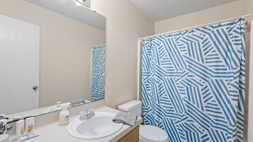 A bathroom with a white sink, mirror, and toilet. There is a shower curtain with a blue and white geometric pattern.