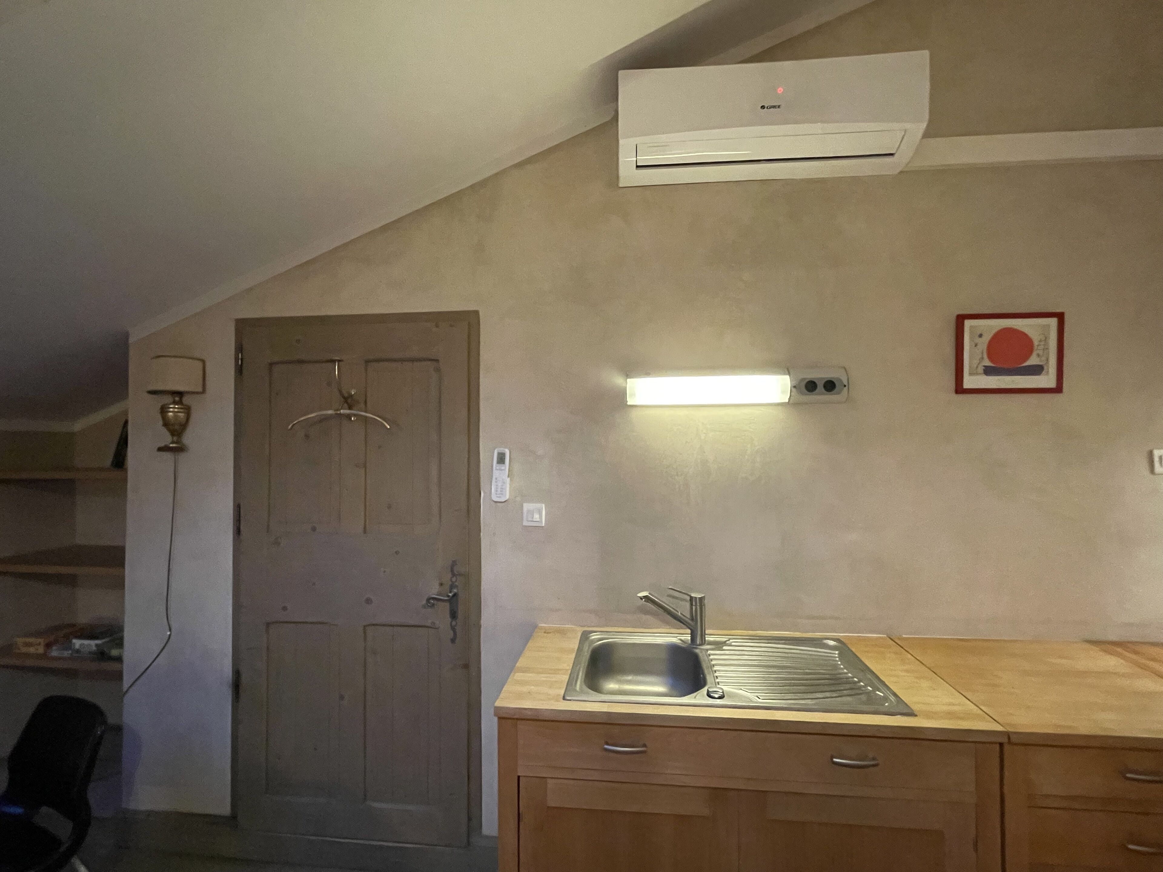A kitchen with a sink, wooden cabinets, an air conditioner, a door, and a wall-mounted light fixture.