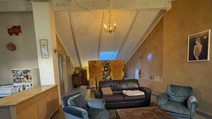 Ein großzügiger Wohnbereich mit hoher Decke, einer Chandelier, einem Sofa, zwei Sesseln, einem Couchtisch und einem kleinen Beistelltisch.