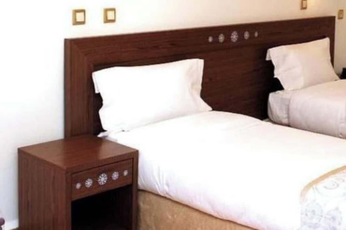 Un dormitorio con cabecera de madera, una cama individual con ropa de cama blanca y una mesita de noche con cajón.