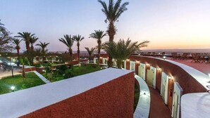A hotel corridor with palm trees and a view of the sea at dusk. - Gourara Hotel  (Timimoun)