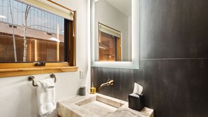 Un bagno con lavabo in marmo, un asciugamano appeso al muro, uno specchio e una finestra con persiane.