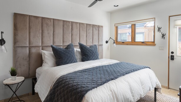 Camera da letto con un letto grande, una ventola a soffitto, una finestra con persiane e un tavolino con una pianta.