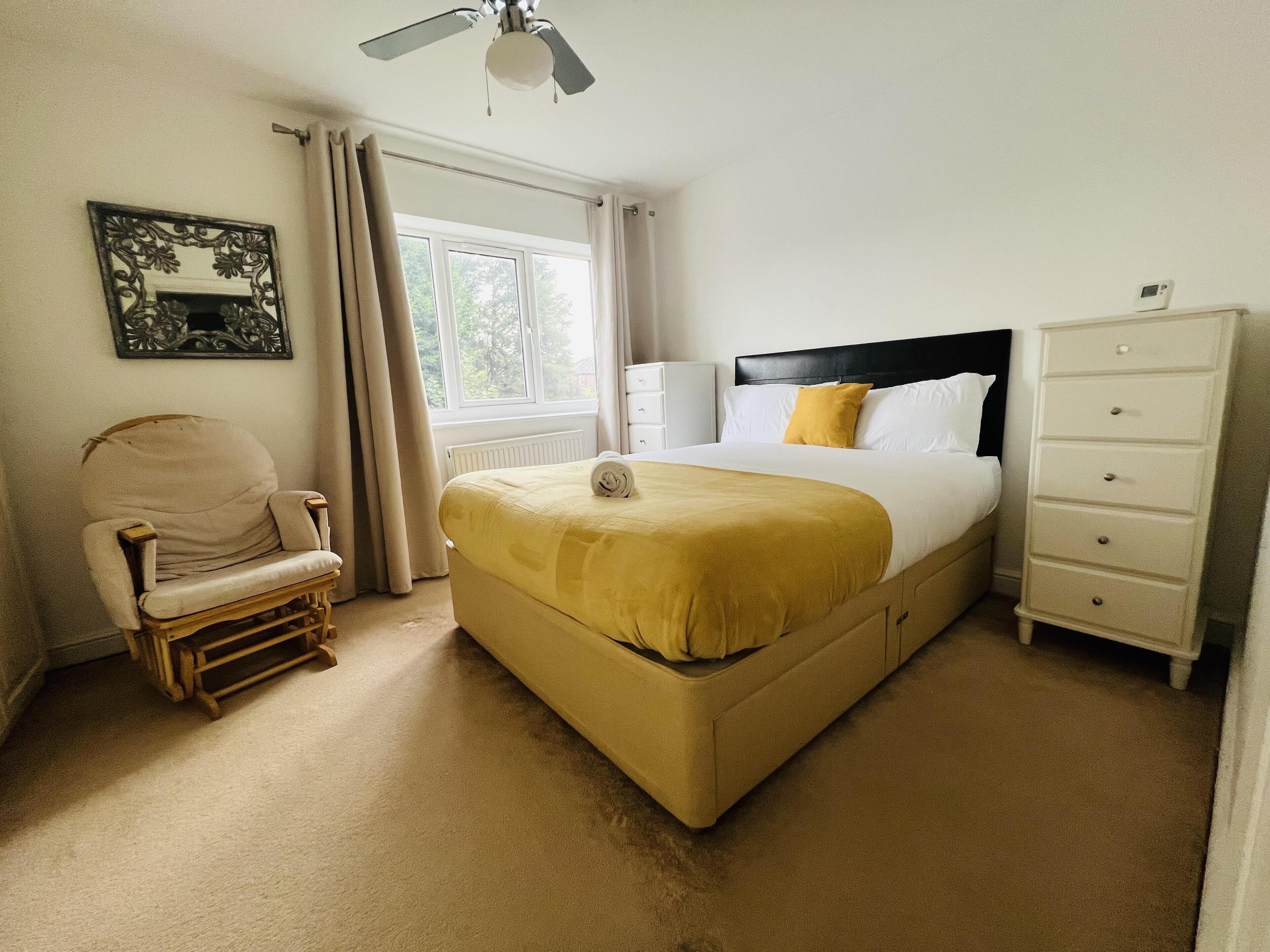Une chambre à coucher comprenant un lit, une chaise, une commode, un ventilateur de plafond et une fenêtre.