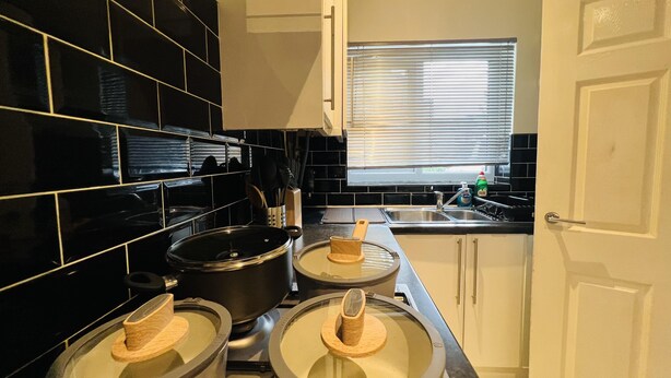 A modern kitchen with black tiled backsplash, stainless steel appliances, and a window with blinds. - Charming 3-bed House in Levenshulme, Manchester (Manchester)