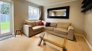 A living room with a beige sectional sofa, a glass coffee table, and a large mirror on the wall. - Charming 3-bed House in Levenshulme, Manchester (Manchester)
