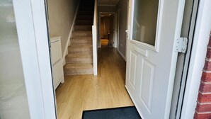 A narrow hallway with a wooden staircase leading to a door with a frosted glass panel. - Charming 3-bed House in Levenshulme, Manchester (Manchester)