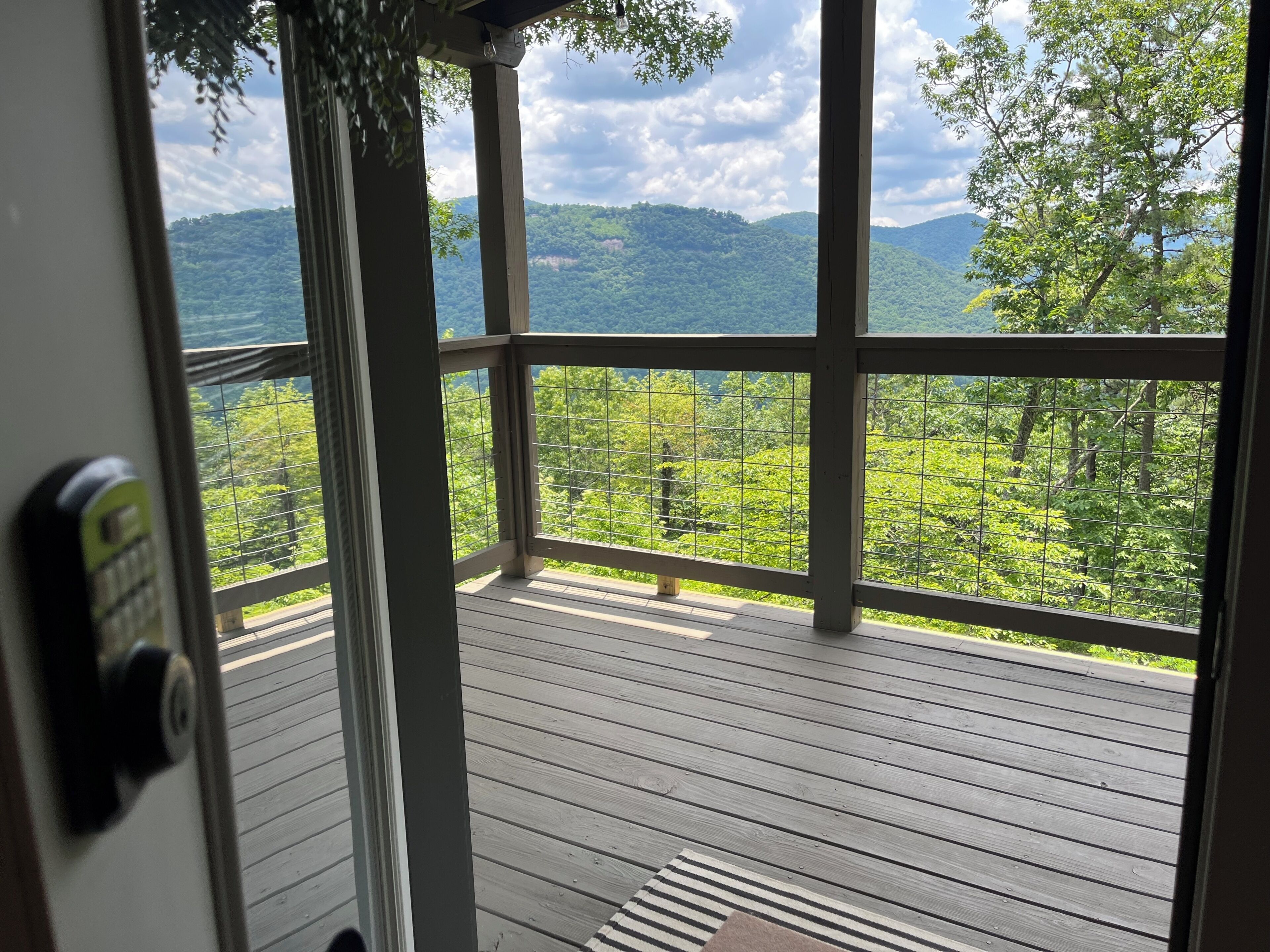 Une terrasse en bois avec une rambarde en métal, donnant sur un paysage boisé.