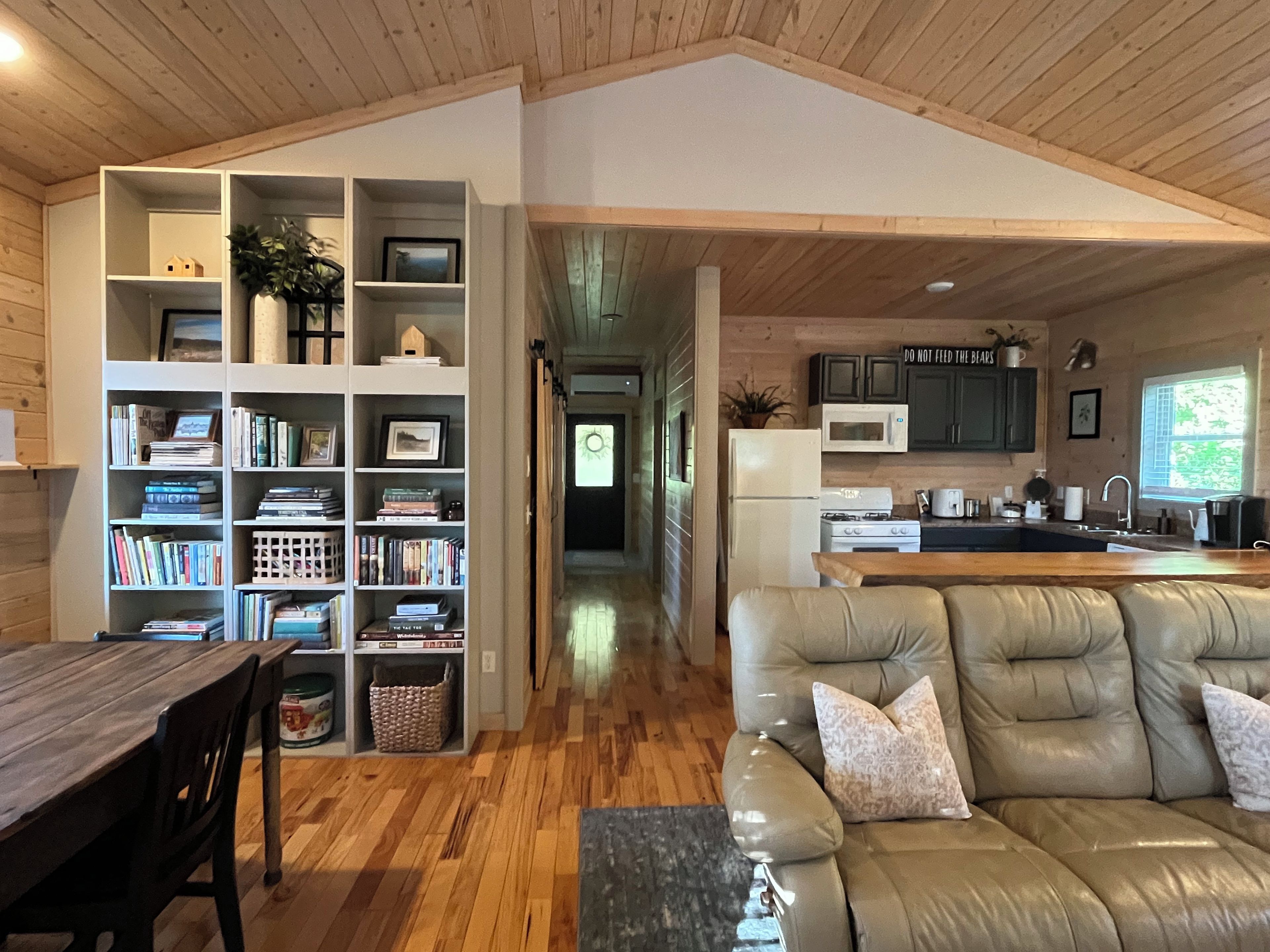 A spacious living area with a leather sofa, wooden flooring, and a kitchen with modern appliances.