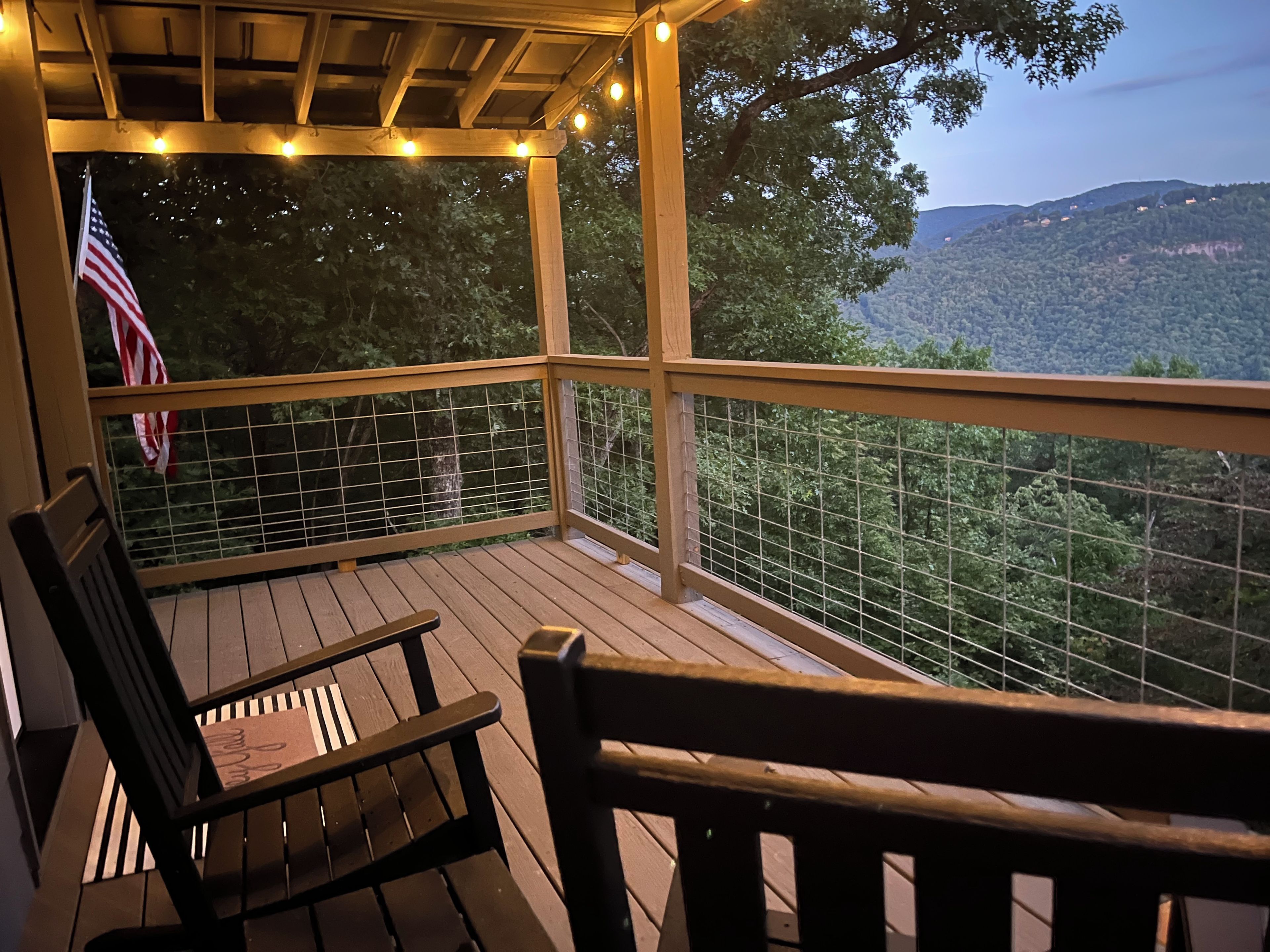 Une terrasse en bois offrant une vue sur une colline boisée, avec un drapeau américain et un banc.
