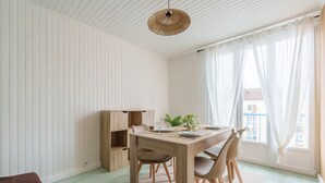 A dining area with a wooden table and chairs, a hanging light fixture, and a view of the outside through large windows.