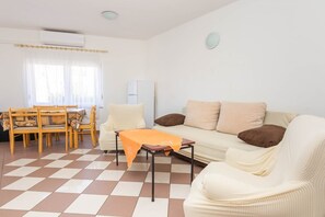 A living room with a checkered floor, a sofa, a table with an orange tablecloth, and a dining area with chairs and a table.