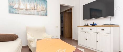A room with a bed, a chair, a table with a tablecloth, a TV on the wall, and a cabinet.