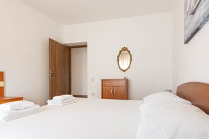 Una habitación de hotel con una cama, un armario de madera, un espejo y una puerta que da a otra estancia.