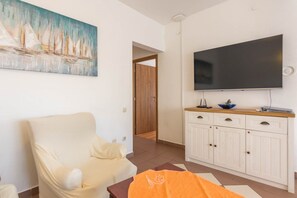 A living room with a white sofa, a flat-screen TV, a cabinet, and a painting on the wall.